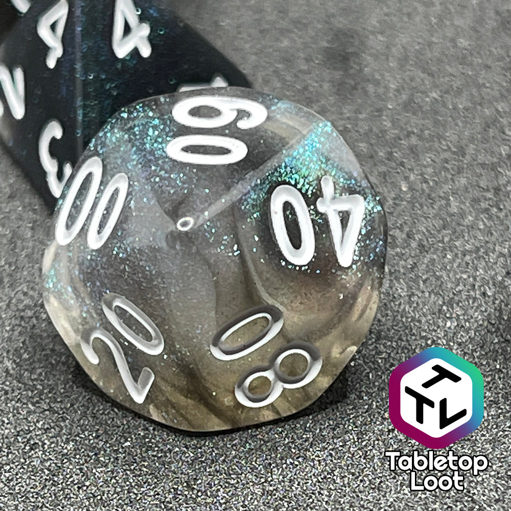A close up of the percentile die from the Black Moonstone 7 piece dice set from Tabletop Loot with swirls of black and teal iridescent glitter, inked in white.