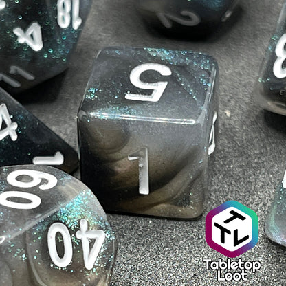 A close up of the D6 from the Black Moonstone 7 piece dice set from Tabletop Loot with swirls of black and teal iridescent glitter, inked in white.