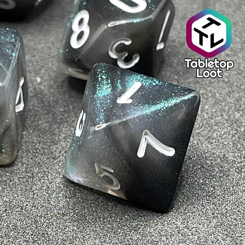 A close up of the D8 from the Black Moonstone 7 piece dice set from Tabletop Loot with swirls of black and teal iridescent glitter, inked in white.