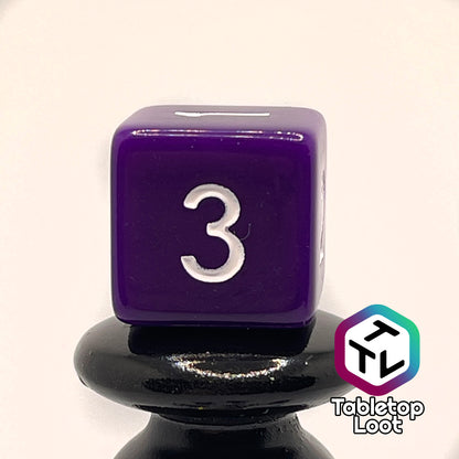 A close up of the D6 from the Blackberries 7 piece dice set; solid purple with white numbering.