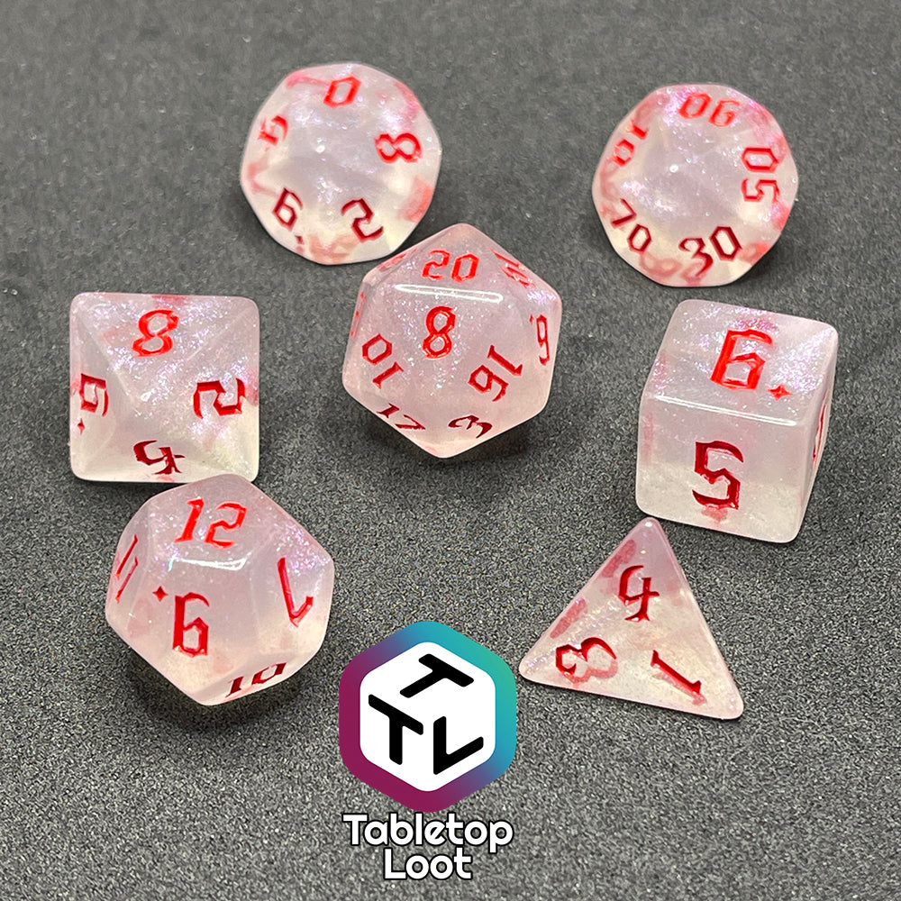 Translucent set of 7 polyhedral dice with iridescent micro-glitter and red numbers.
