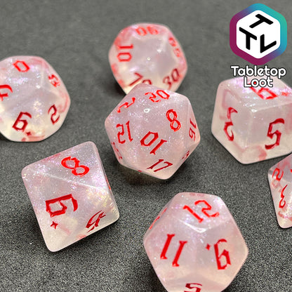 Translucent set of 7 polyhedral dice with iridescent micro-glitter and red numbers.