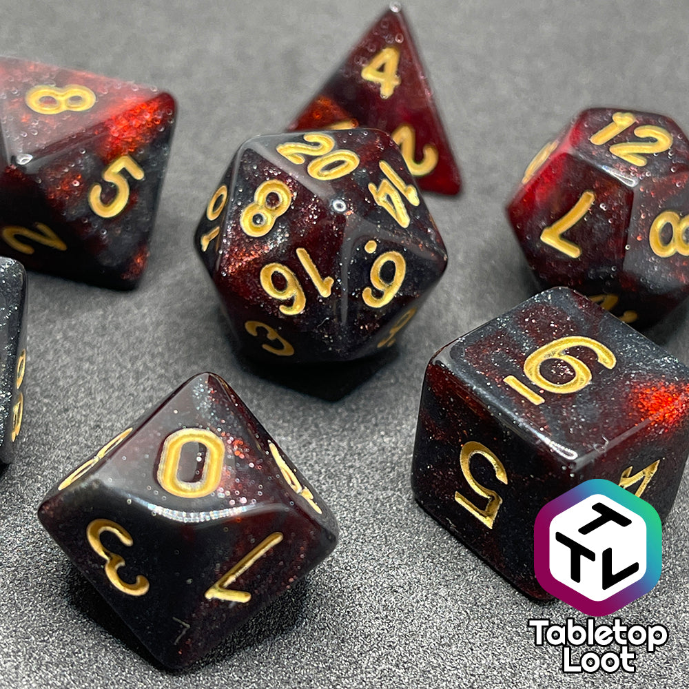 A close up of the Blood Lust 7 piece dice set from Tabletop Loot with swirls of dark glittery red which looks almost black and gold numbering.