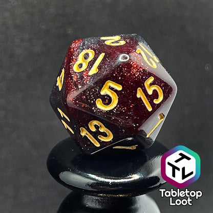 A close up of the D20 from the Blood Lust 7 piece dice set from Tabletop Loot with swirls of dark glittery red which looks almost black and gold numbering.