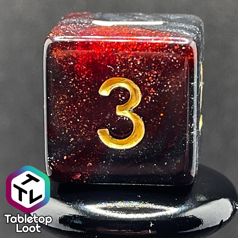 A close up of the D6 from the Blood Lust 7 piece dice set from Tabletop Loot with swirls of dark glittery red which looks almost black and gold numbering.