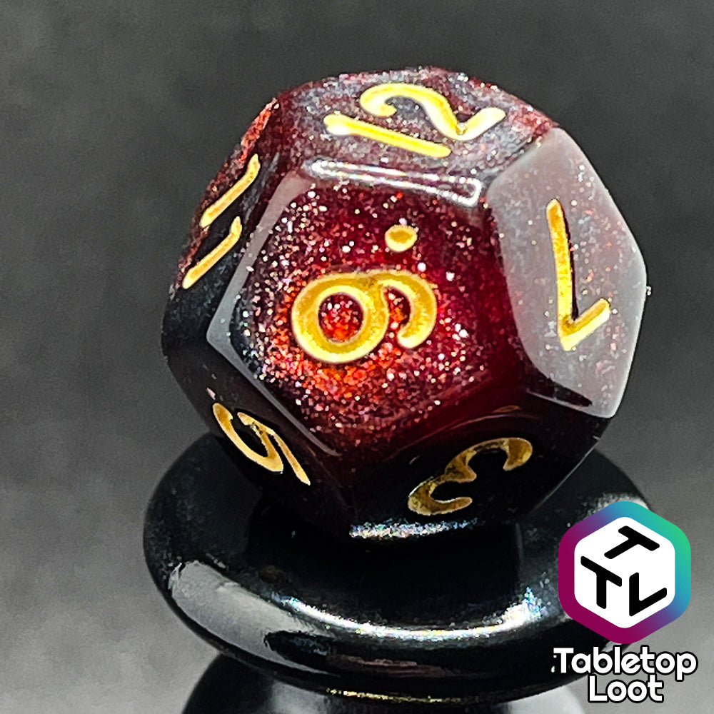 A close up of the D12 from the Blood Lust 7 piece dice set from Tabletop Loot with swirls of dark glittery red which looks almost black and gold numbering.