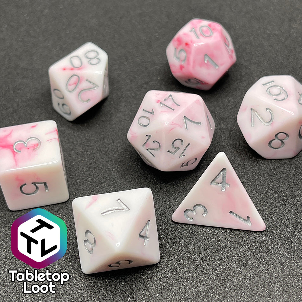 A close up of the Blood Oath 7 piece dice set from Tabletop Loot; opaque white with swirls of red peeking out and silver numbers.