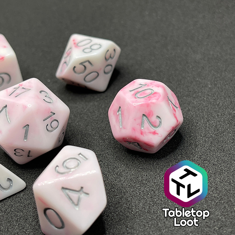 A close up of the D12 from the Blood Oath 7 piece dice set from Tabletop Loot; opaque white with swirls of red peeking out and silver numbers.