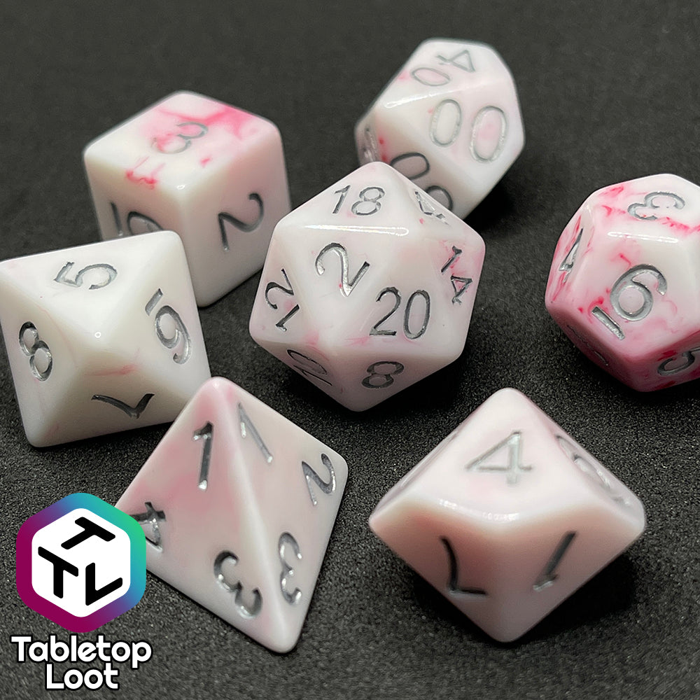 A close up of the Blood Oath 7 piece dice set from Tabletop Loot; opaque white with swirls of red peeking out and silver numbers.