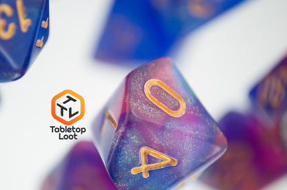 A close up of the Blue Enchantress 7 piece dice set from Tabletop Loot with shimmering shades of pink, purple, and blue swirling resin and gold numbering.