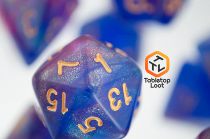 A close up of the D20 from the Blue Enchantress 7 piece dice set from Tabletop Loot with shimmering shades of pink, purple, and blue swirling resin and gold numbering.