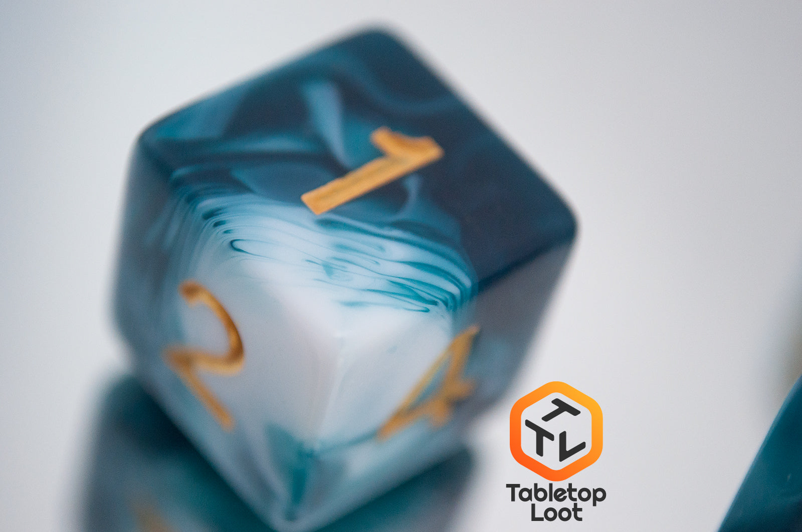 A close up of the D6 from the Blue Ink 7 piece dice set from Tabletop Loot with swirls of ocean blue and white resin and gold numbering.