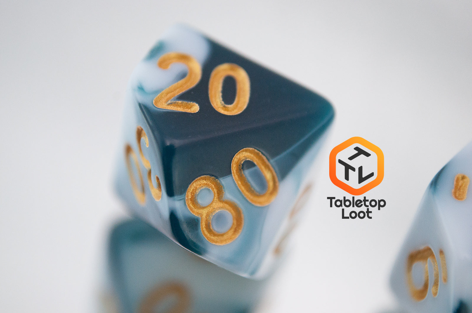 A close up of the percentile die from the Blue Ink 7 piece dice set from Tabletop Loot with swirls of ocean blue and white resin and gold numbering.