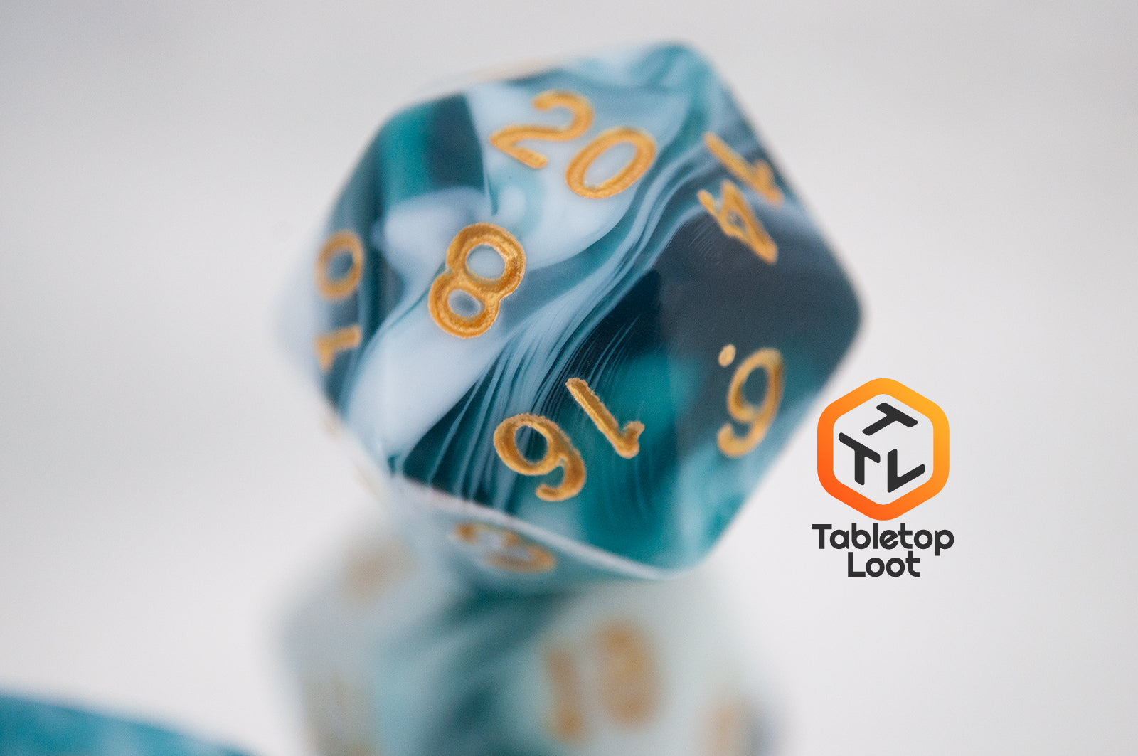 A close up of the D20 from the Blue Ink 7 piece dice set from Tabletop Loot with swirls of ocean blue and white resin and gold numbering.