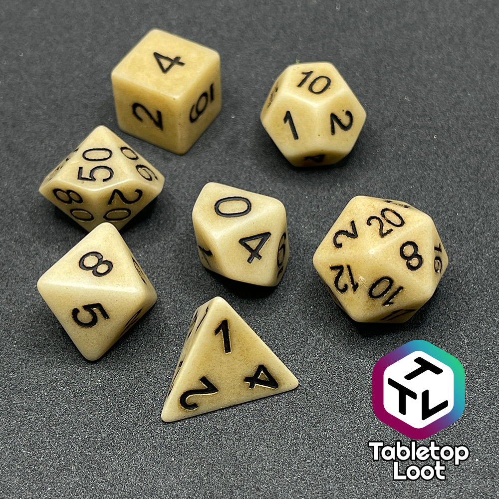The Bones of the Earth 7 piece dice set from Tabletop Loot with a bone colored and textured appearance and black numbering.