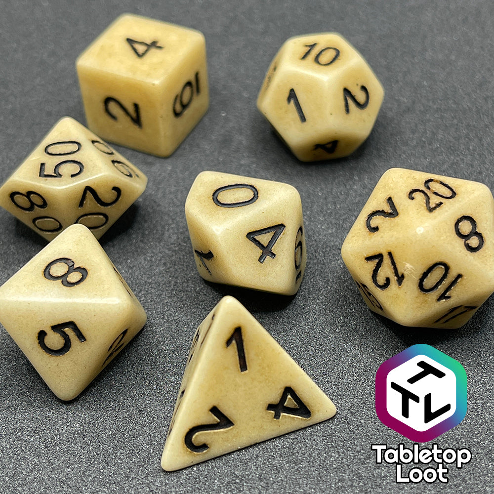 The Bones of the Earth 7 piece dice set from Tabletop Loot with a bone colored and textured appearance and black numbering.