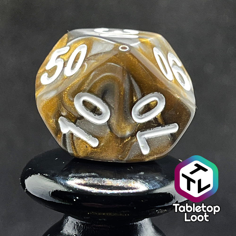 A close up of the percentile die from the Bronze Dragon 7 piece dice set from Tabletop Loot with swirls of pearlescent bronze and silver and silver numbering.