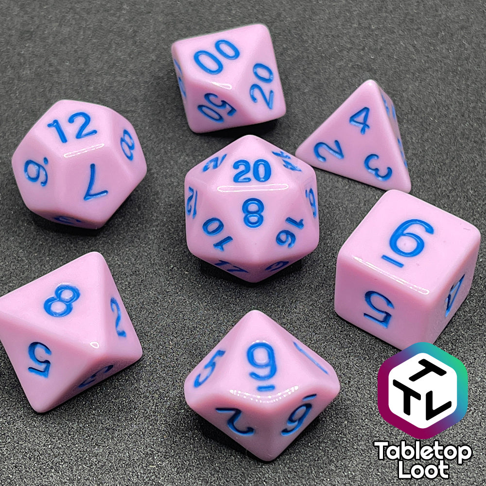 A close up of the Berry Bubblegum 7 piece dice set from Tabletop Loot with blue numbering on solid pastel pink sides.