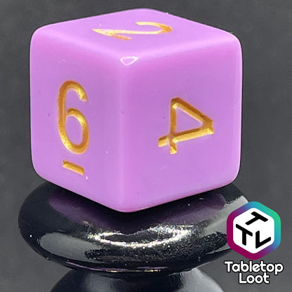 A close up of the D6 from the Carnations 7 piece dice set from Tabletop Loot with gold numbering on solid pink faces.
