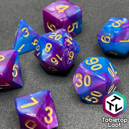 A close up of the Carnival 7 piece dice set from Tabletop Loot with swirls of blue and purple and gold numbering.