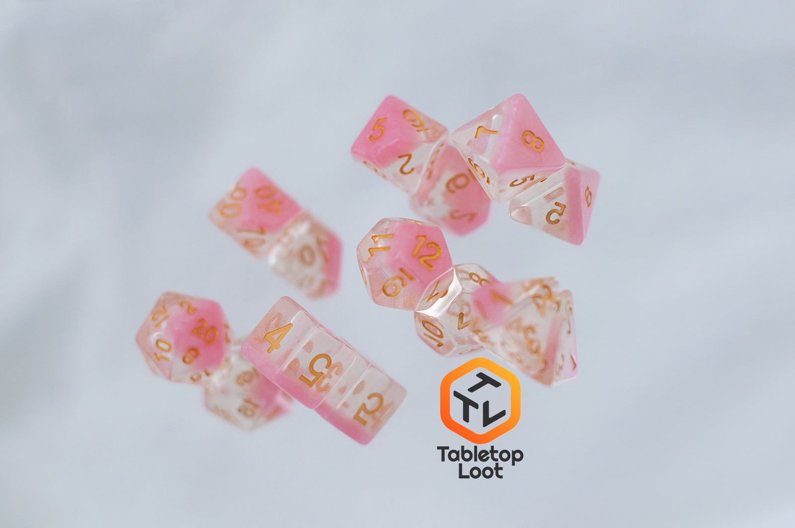 The Cherry Blossom 7 piece dice set from Tabletop Loot with a layer of glittery pink resin in clear glittery resin and gold numbers.