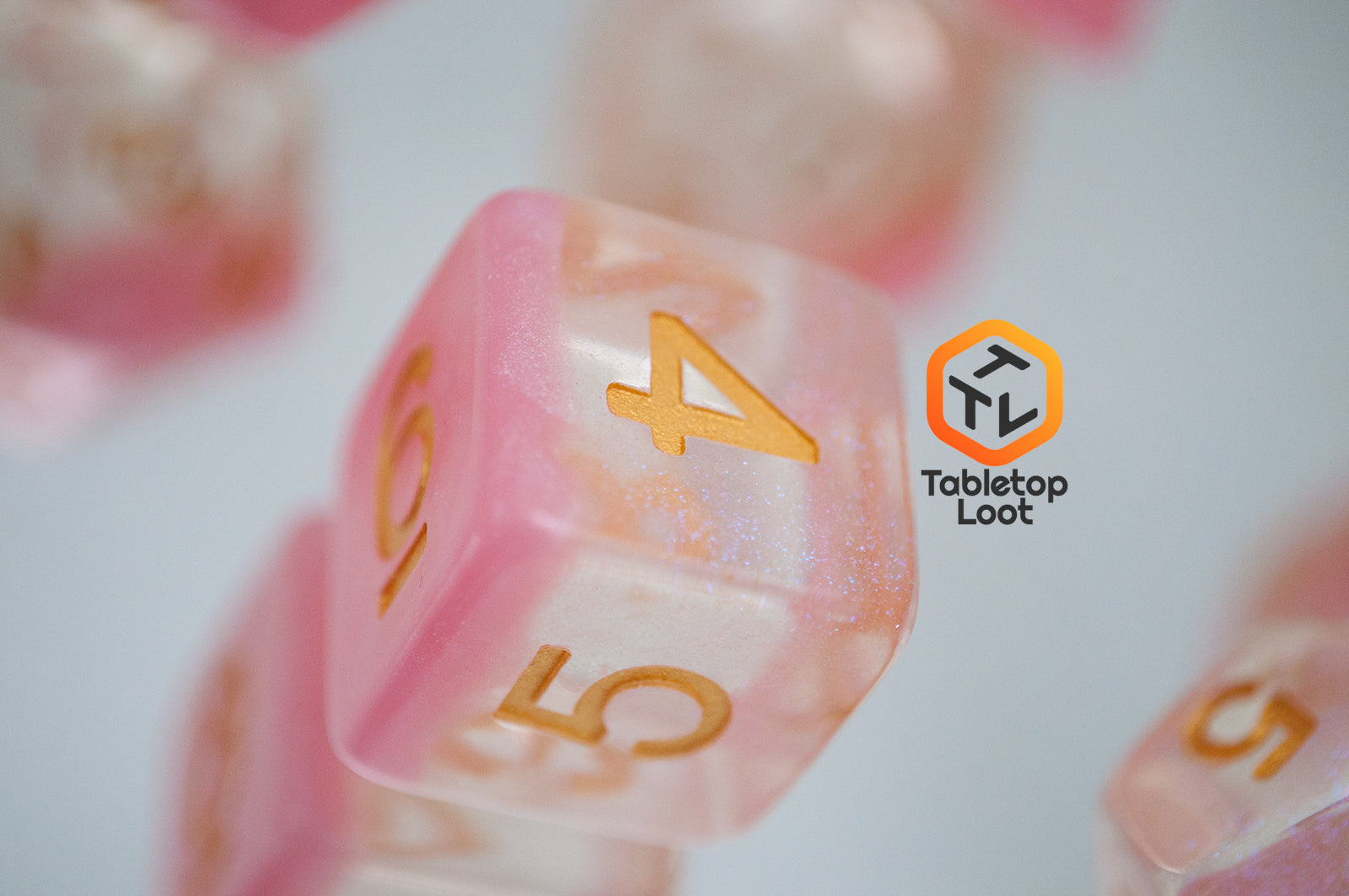 A close up of the D6 from the Cherry Blossom 7 piece dice set from Tabletop Loot with a layer of glittery pink resin in clear glittery resin and gold numbers.