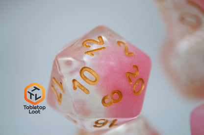 A close up of the D20 from the Cherry Blossom 7 piece dice set from Tabletop Loot with a layer of glittery pink resin in clear glittery resin and gold numbers.