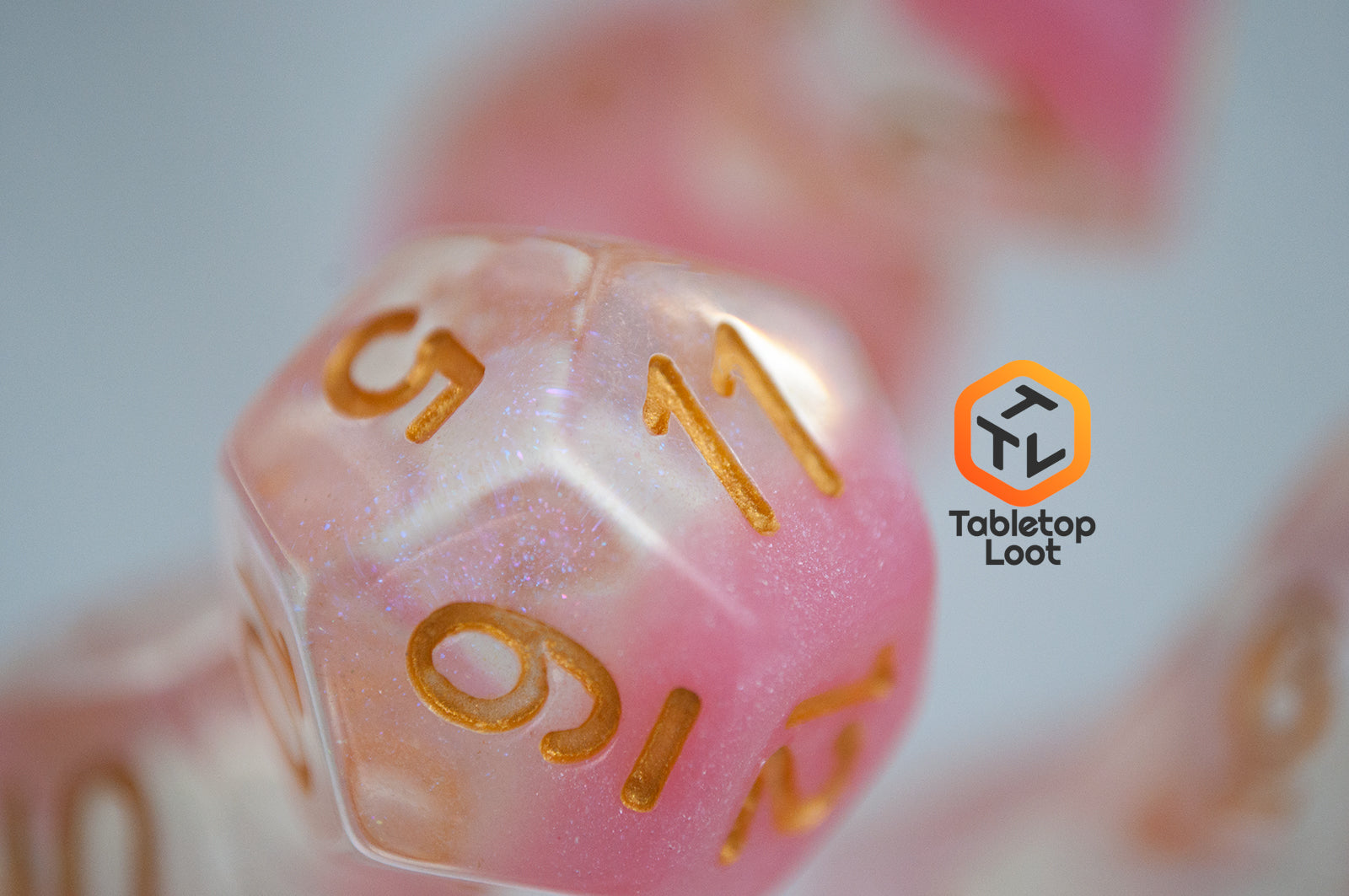 A close up of the D12 from the Cherry Blossom 7 piece dice set from Tabletop Loot with a layer of glittery pink resin in clear glittery resin and gold numbers.