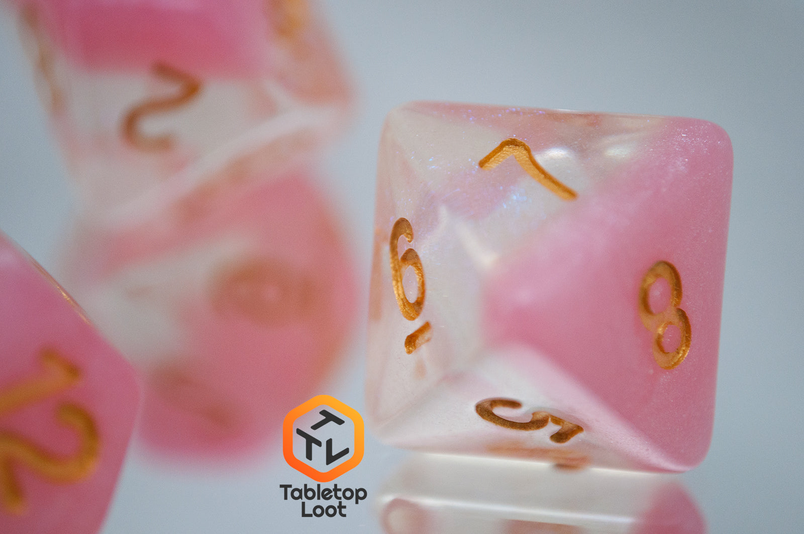 A close up of the D8 from the Cherry Blossom 7 piece dice set from Tabletop Loot with a layer of glittery pink resin in clear glittery resin and gold numbers.