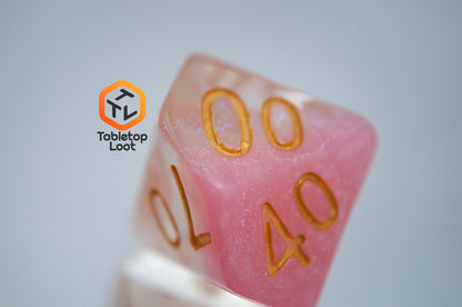 A close up of the percentile die from the Cherry Blossom 7 piece dice set from Tabletop Loot with a layer of glittery pink resin in clear glittery resin and gold numbers.
