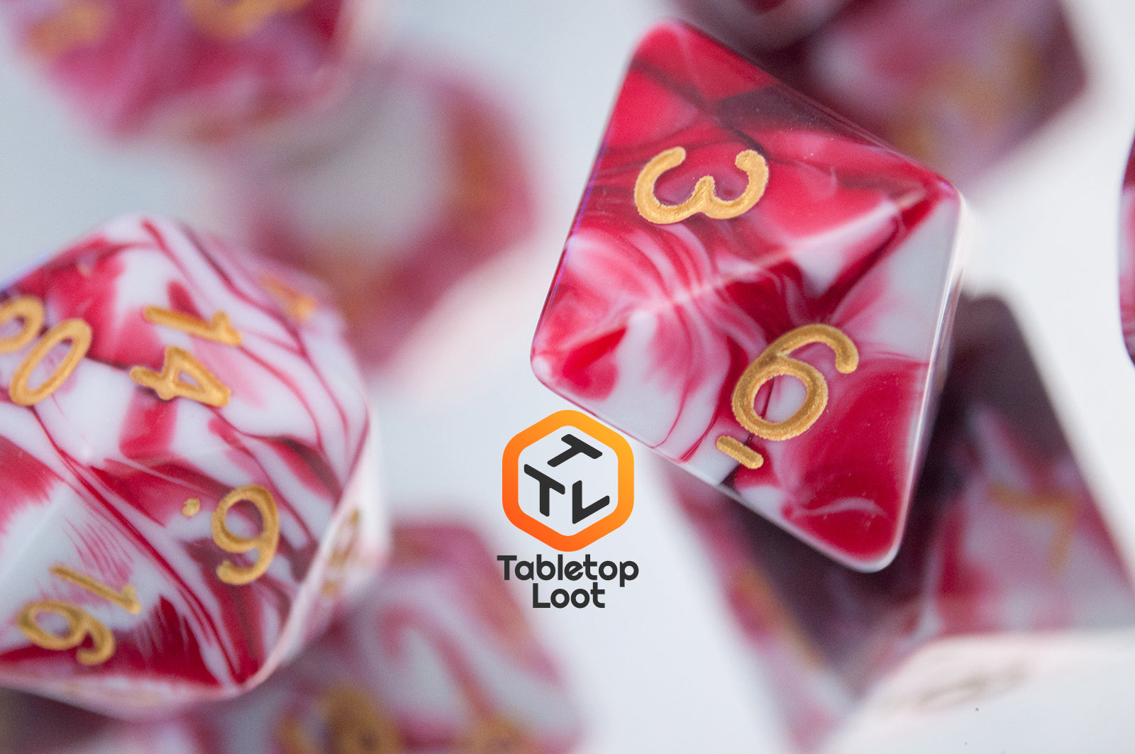 A close up of the Strawberry Sundae 7 piece dice set from Tabletop Loot with swirls of red, pink, and white and gold ink.