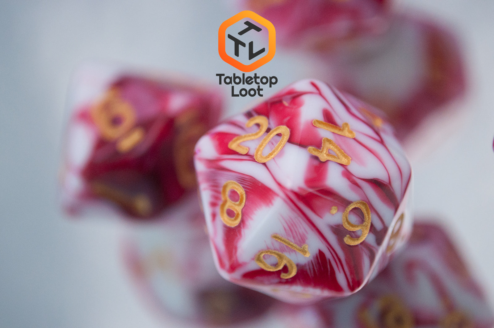 A close up of the D20 from the Strawberry Sundae 7 piece dice set from Tabletop Loot with swirls of red, pink, and white and gold ink.