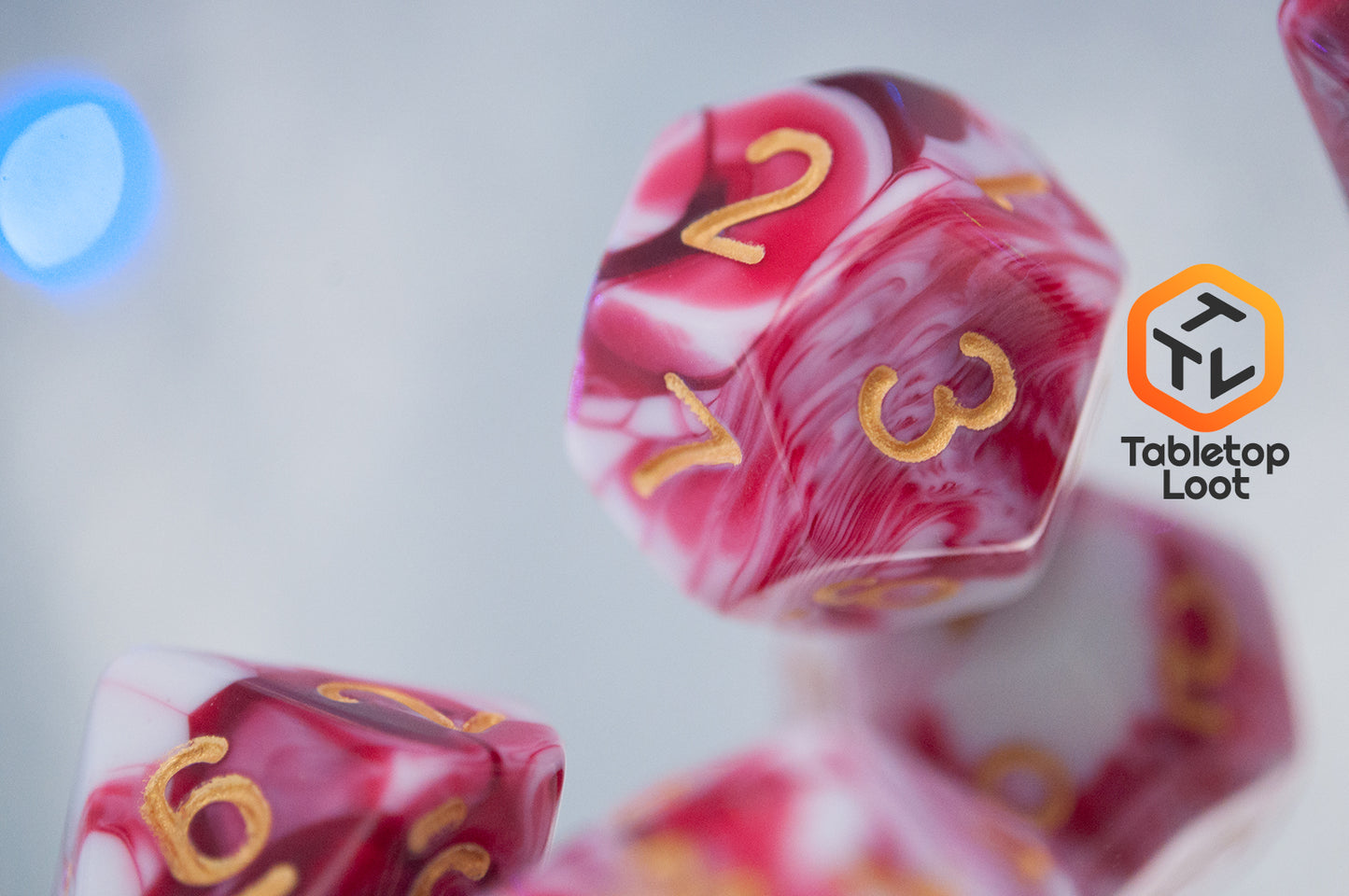 A close up of the D12 from the Strawberry Sundae 7 piece dice set from Tabletop Loot with swirls of red, pink, and white and gold ink.
