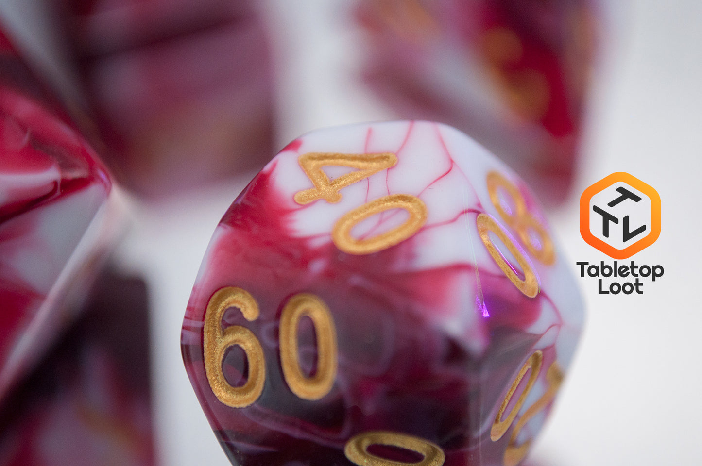 A close up of the percentile die from the Strawberry Sundae 7 piece dice set from Tabletop Loot with swirls of red, pink, and white and gold ink.