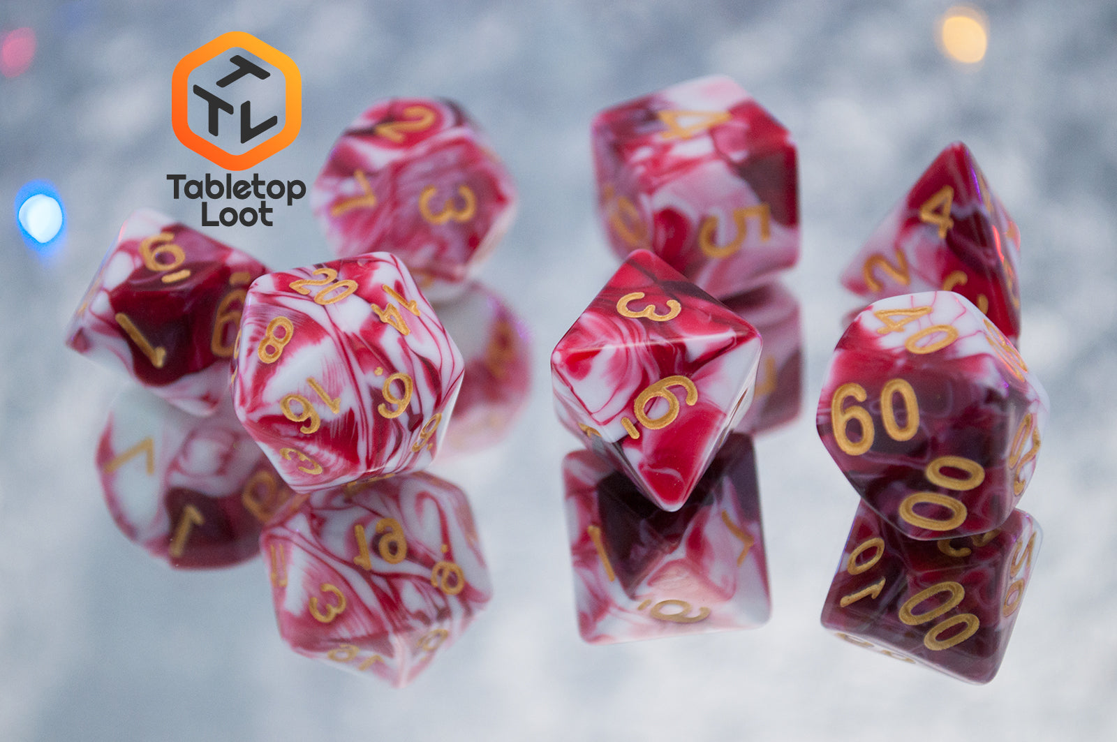 The Strawberry Sundae 7 piece dice set from Tabletop Loot with swirls of red, pink, and white and gold ink.