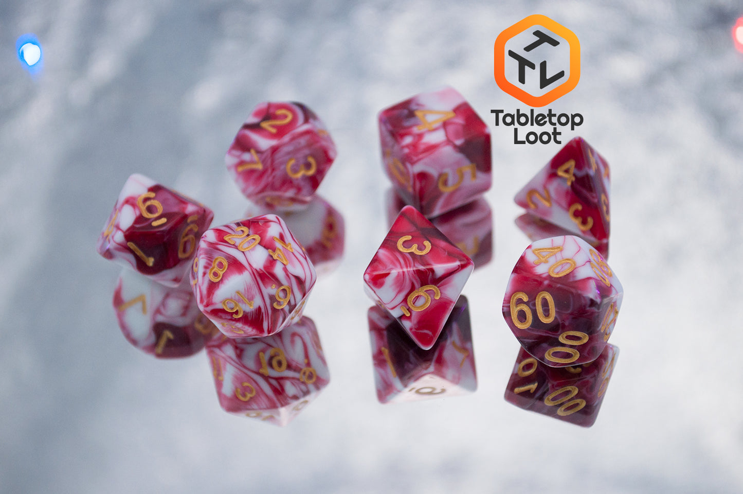 The Strawberry Sundae 7 piece dice set from Tabletop Loot with swirls of red, pink, and white and gold ink.
