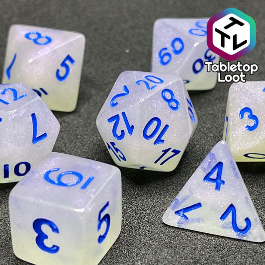 A close up of the Clairvoyance 7 piece dice set from Tabletop Loot with royal blue numbering on milky shimmery dice.