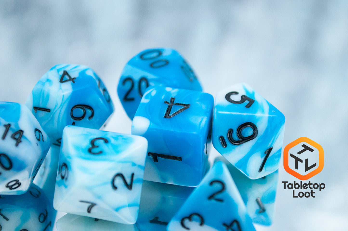 A close up of the Cloudy Sky 7 piece dice set from Tabletop Loot with swirls of bright blue and white resin and black numbering.