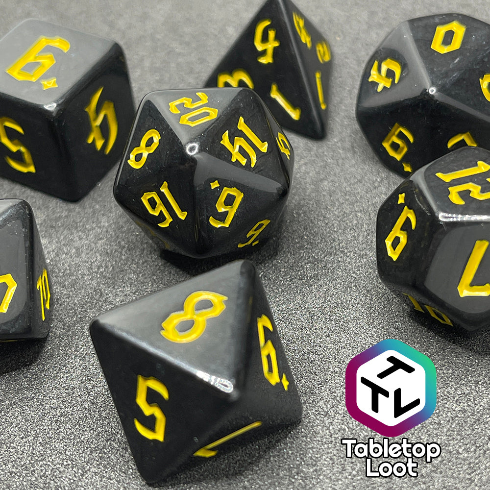 A close up of the Construct 7 piece dice set from Tabletop Loot with bright yellow bold gothic numbers on a highly reflective solid black surface.