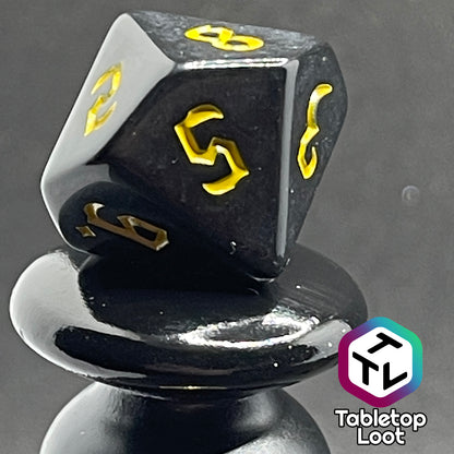 A close up of the D10 from the Construct 7 piece dice set from Tabletop Loot with bright yellow bold gothic numbers on a highly reflective solid black surface.