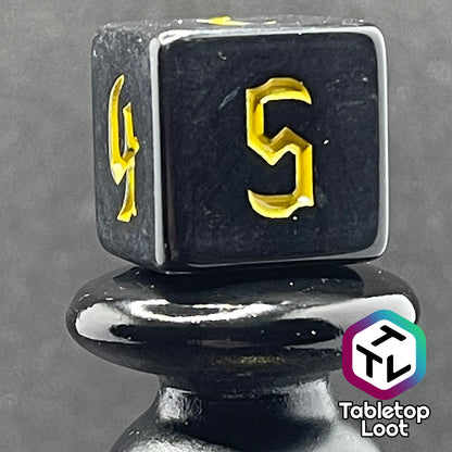 A close up of the D6 from the Construct 7 piece dice set from Tabletop Loot with bright yellow bold gothic numbers on a highly reflective solid black surface.