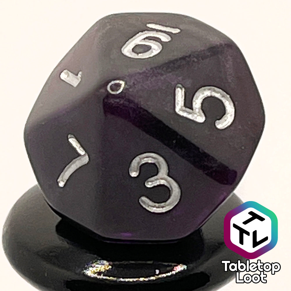A close up of the D10 from the Darkness 7 piece dice set from Tabletop Loot; translucent purple so dark it looks black except where the light peeks through in corners, inked in silver.
