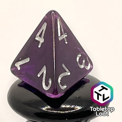 A close up of the D4 from the Darkness 7 piece dice set from Tabletop Loot; translucent purple so dark it looks black except where the light peeks through in corners, inked in silver.