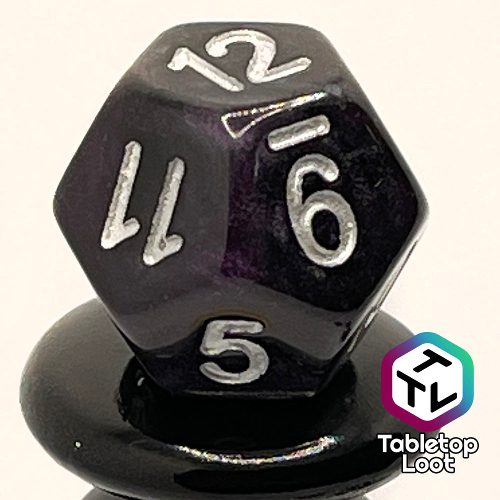 A close up of the D12 from the Darkness 7 piece dice set from Tabletop Loot; translucent purple so dark it looks black except where the light peeks through in corners, inked in silver.
