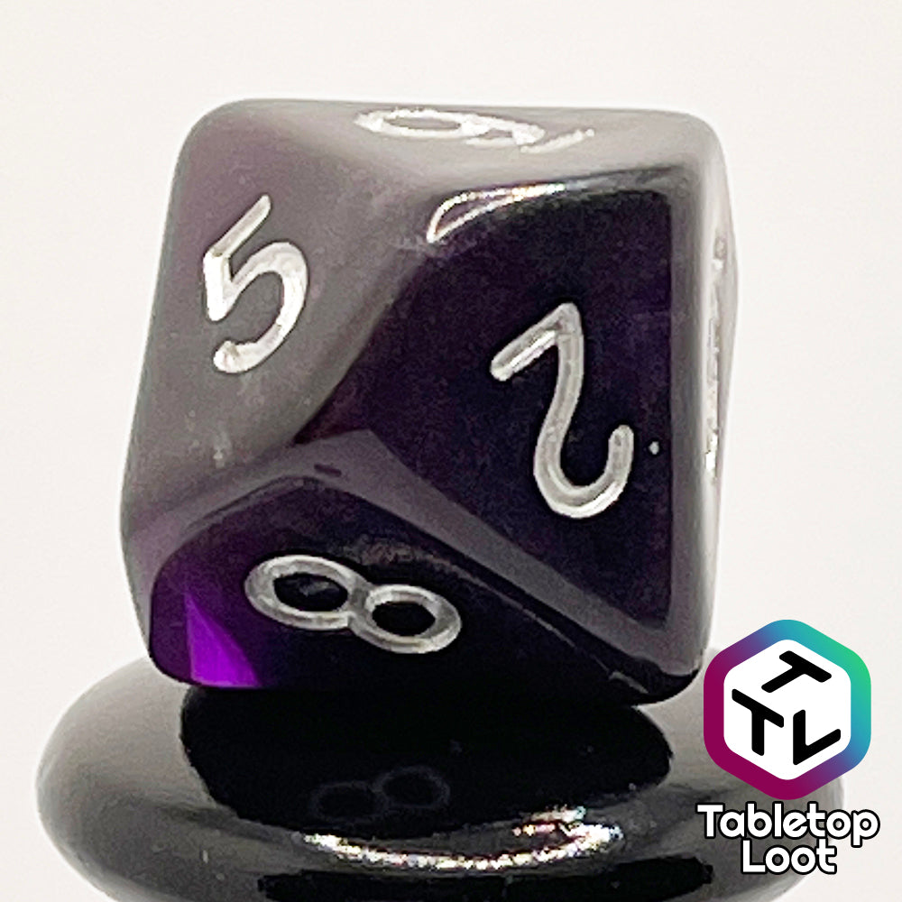A close up of the D10 from the Darkness 7 piece dice set from Tabletop Loot; translucent purple so dark it looks black except where the light peeks through in corners, inked in silver.