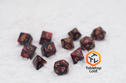 The Demon Stones 11 piece dice set from Tabletop Loot with deep red swirled with black resin and gold numbering.