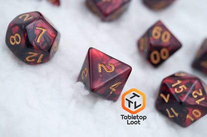 A close up of the Demon Stones 11 piece dice set from Tabletop Loot with deep red swirled with black resin and gold numbering.