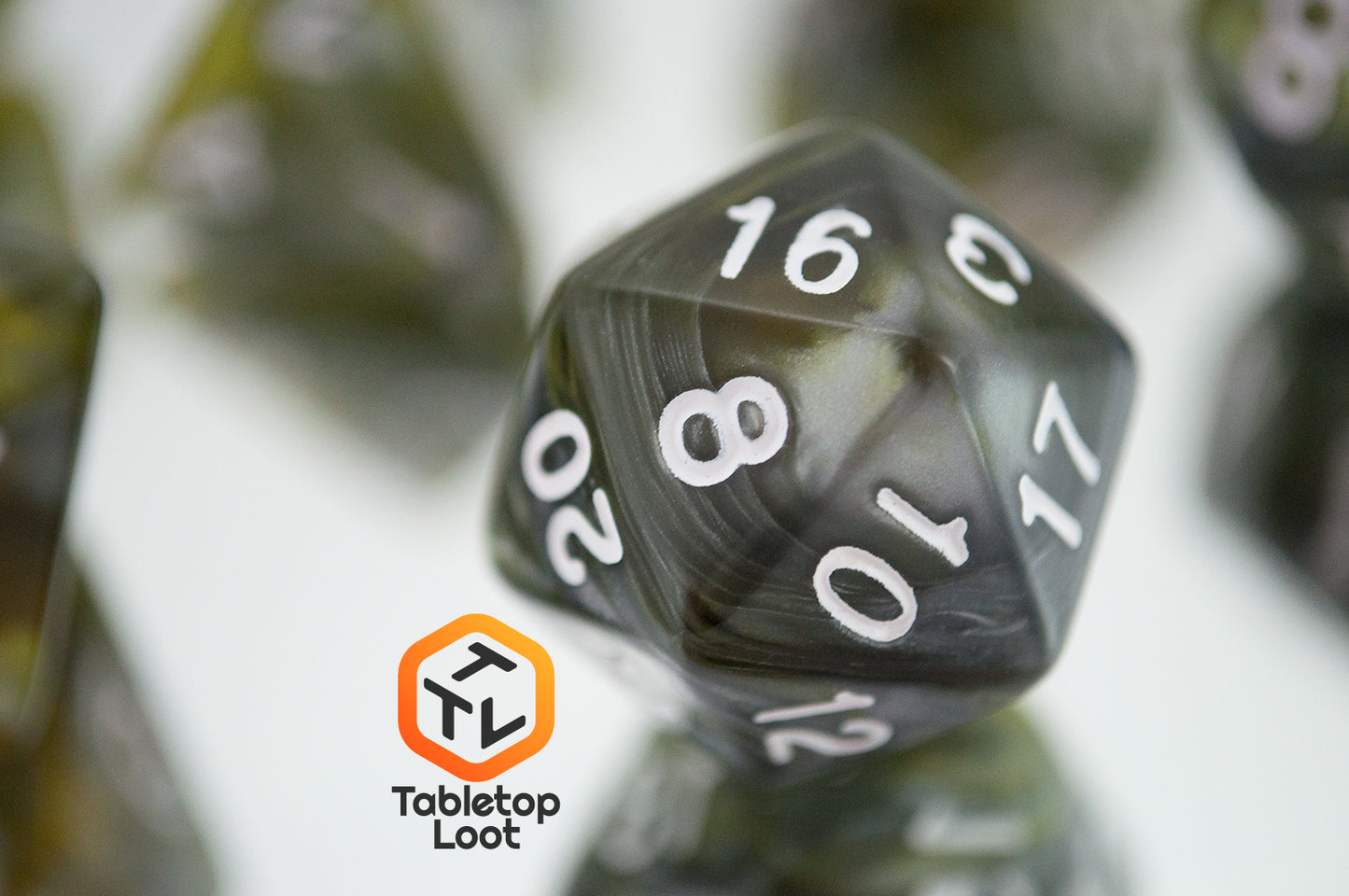 A close up of the D20 from the Disintegrate 7 piece dice set from Tabletop Loot with swirls of silver and gold and white numbering.