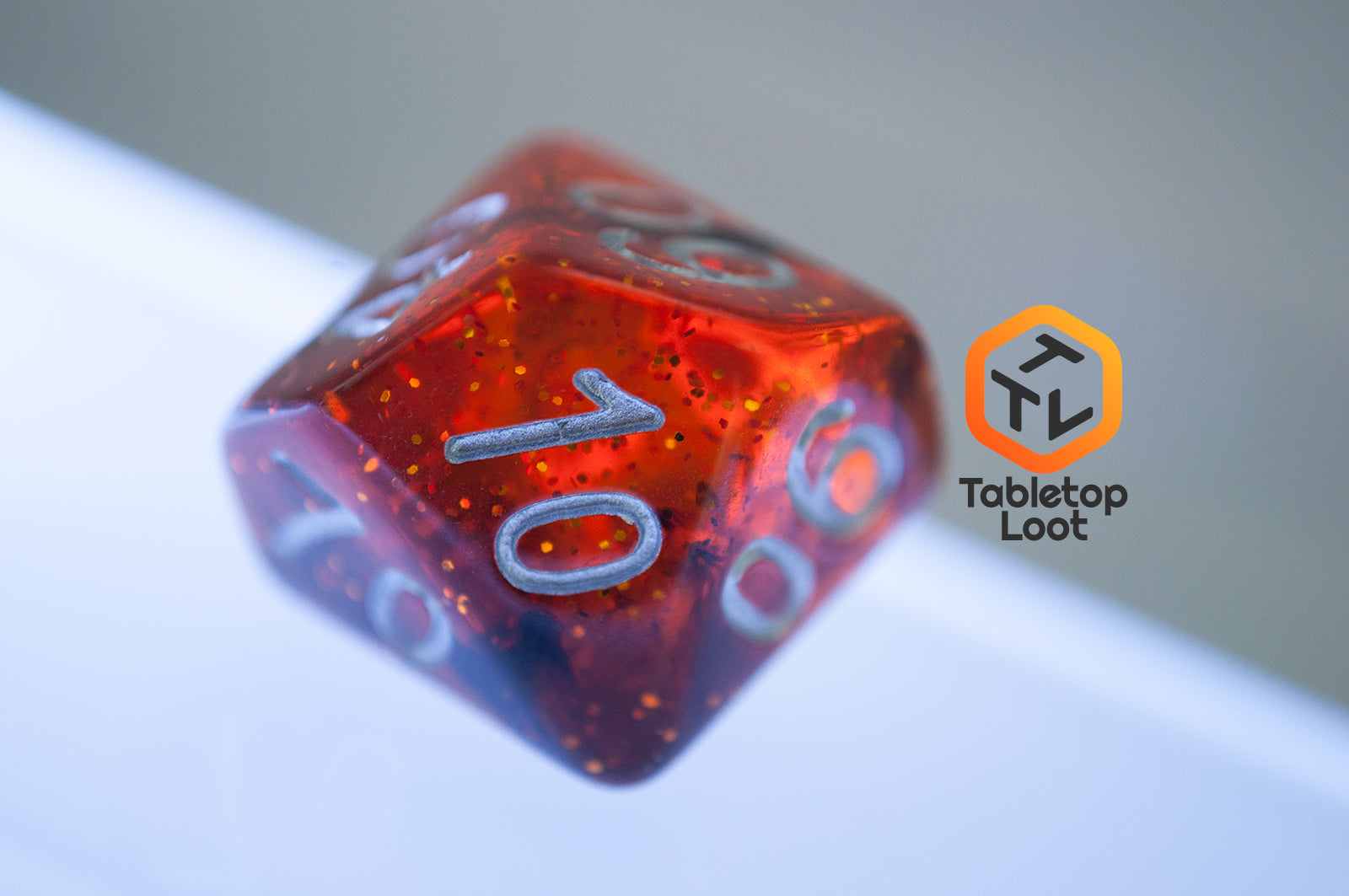 A close up of the percentile die from the Dissonant Whispers 7 piece dice set from Tabletop Loot with swirls of black in sparkling amber color, inked in silver.