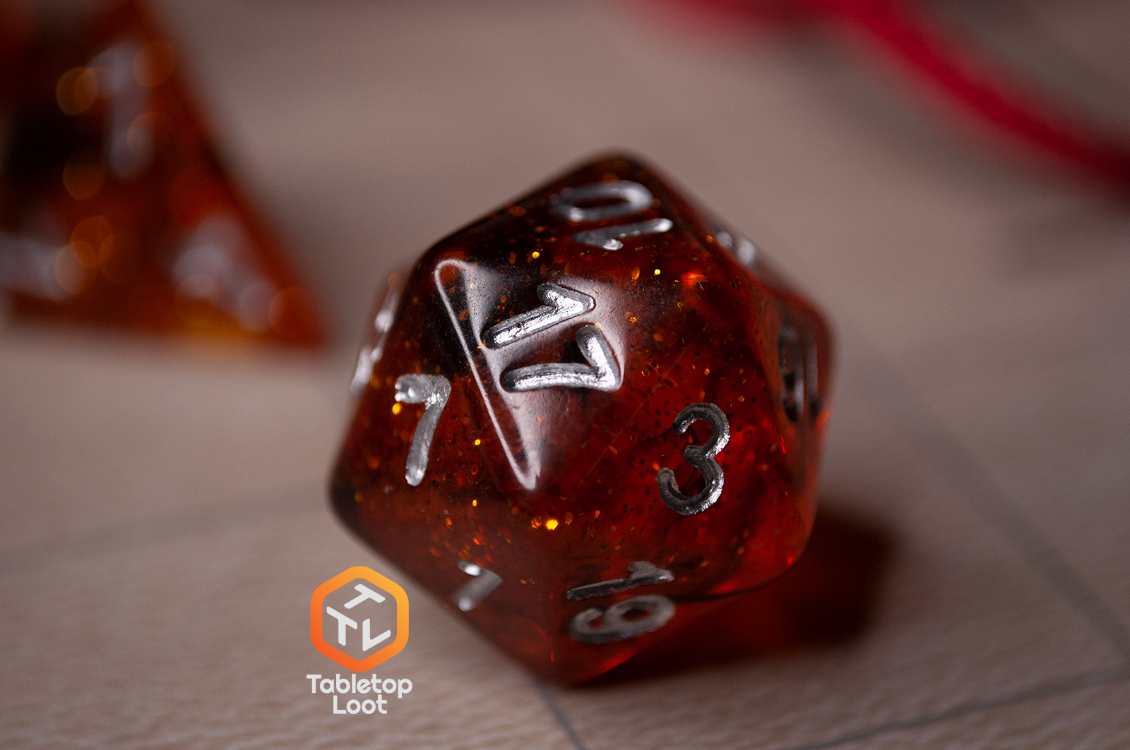 A close up of the D20 from the Dissonant Whispers 7 piece dice set from Tabletop Loot with swirls of black in sparkling amber color, inked in silver.